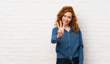 Beyaz tuğla duvar üzerinde Redhead kadın mutlu ve parmakları ile üç sayma