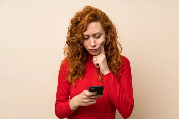 Redhead woman with turtleneck sweater using mobile phone