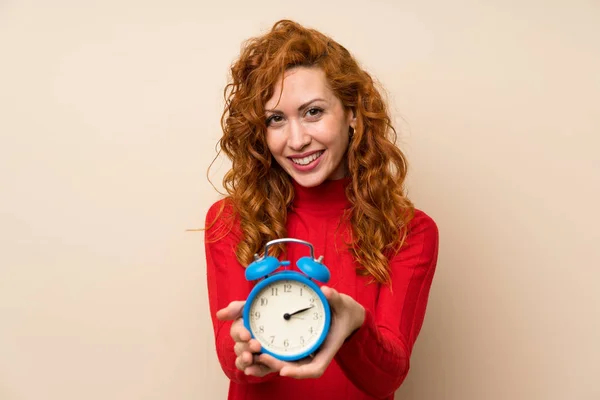 Redhead woman with turtleneck sweater holding vintage alarm clock