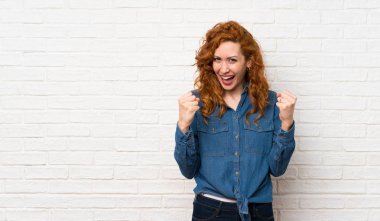 Beyaz tuğla duvar üzerinde Redhead kadın kazanan pozisyonda bir zafer kutluyor