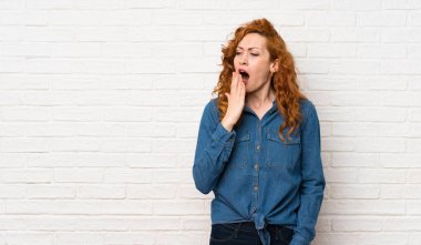 Beyaz tuğla duvar esneme üzerinde Redhead kadın esneme ve el ile geniş açık ağız kapsayan