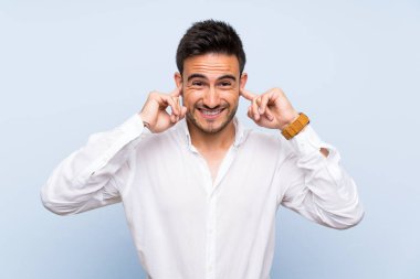 Izole mavi arka plan üzerinde Yakışıklı genç adam sinirli ve kulakları kapsayan