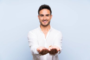 Bir reklam eklemek için avuç üzerinde copyspace hayali tutan izole mavi arka plan üzerinde Yakışıklı genç adam