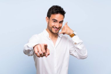 Izole mavi arka plan üzerinde yakışıklı genç adam telefon jest yapma ve ön işaret