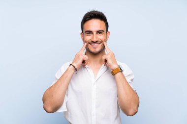 Izole mavi arka plan üzerinde Yakışıklı genç adam mutlu ve hoş bir ifade ile gülümseyen