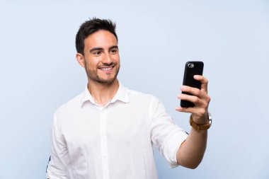 Izole mavi arka plan üzerinde yakışıklı genç adam selfie yapma