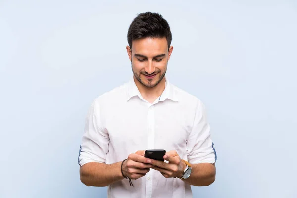 Joven Guapo Sobre Fondo Azul Aislado Enviando Mensaje Con Móvil — Foto de Stock