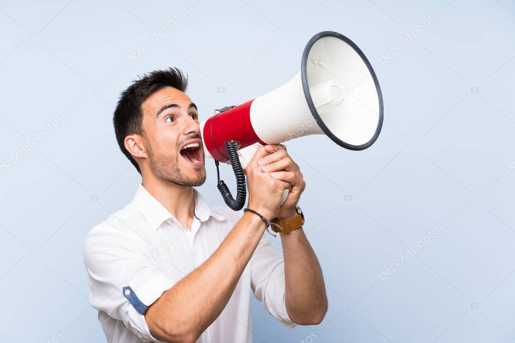 Handsome young man over isolated blue background shouting through a megaphone