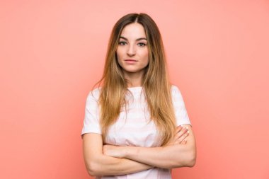 İzole edilmiş pembe duvarda kollarını kavuşturan genç bir kadın.