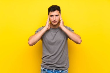 Izole sarı duvar üzerinde Yakışıklı adam sinirli ve kulakları kapsayan