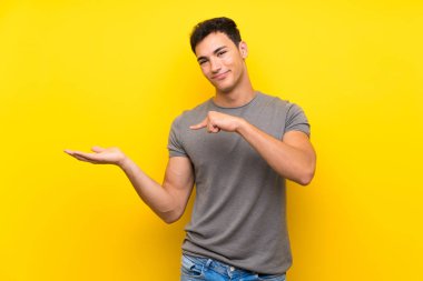 Bir reklam eklemek için avuç üzerinde copyspace hayali tutan izole sarı duvar üzerinde Yakışıklı adam