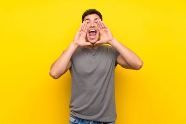 Izole sarı duvar üzerinde Yakışıklı adam bağırarak ve bir şey ilan