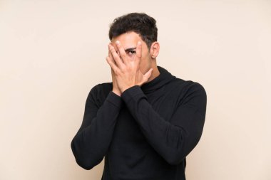 Gözleri kaplayan ve parmaklardan bakan izole arka plan üzerinde Yakışıklı adam