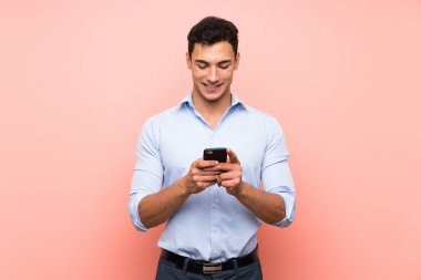 Pembe arka planda yakışıklı bir adam cep telefonuyla mesaj gönderiyor.