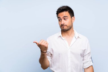 İzole mavi arka plan mutsuz üzerinde yakışıklı genç adam ve yan işaret