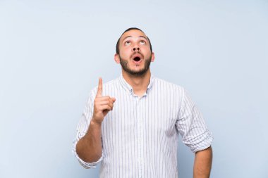 İzole mavi duvar üzerinde Kolombiyalı adam yukarı işaret ve sürpriz