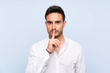Yakışıklı genç adam üzerinde izole mavi arka plan gösteren bir işareti sessizlik jest koymak parmak içinde ağız