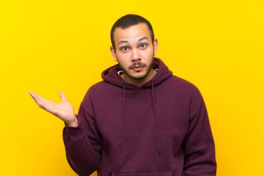 Sarı duvar üzerinde Sweatshirt ile Kolombiyalı adam şüpheler jest yapma