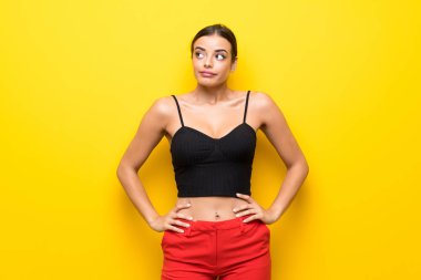 Izole sarı arka plan üzerinde genç kadın yan görünümlü şüpheler jest yapma