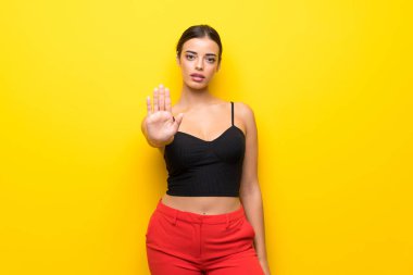 Izole sarı arka plan üzerinde genç kadın stop jest yapma