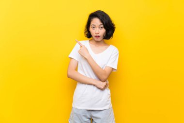 Asya genç kadın üzerinde izole sarı duvar şaşırttı ve işaret yan