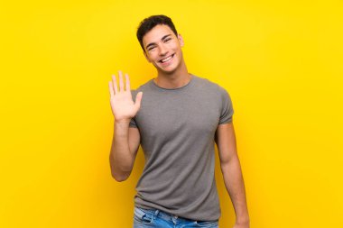 Mutlu ifade ile el ile selamizole sarı duvar üzerinde Yakışıklı adam