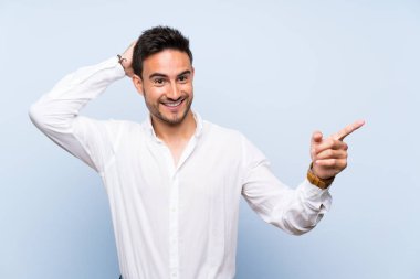 İzole mavi arka plan üzerinde yakışıklı genç adam sürpriz ve tarafına parmak işaret