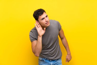 Izole sarı duvar üzerinde yakışıklı adam kulağına el koyarak bir şey dinlerken