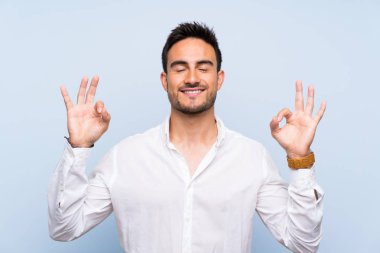 Zen poz içinde izole mavi arka plan üzerinde yakışıklı genç adam