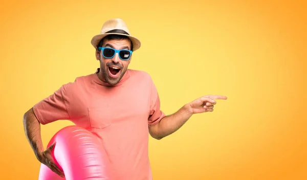 戴着帽子和太阳镜的男人指着一边 一边展示产品 一边以自信的姿势在橙色背景上微笑 — 图库照片