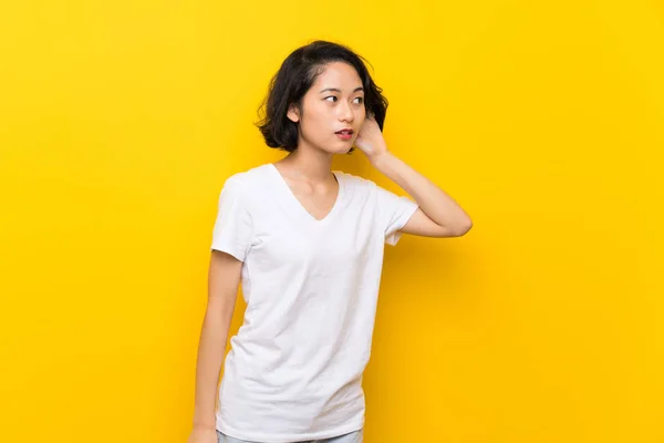 Азіатські Молода Жінка Над Ізольованою Жовта Стіна Прислухаючись Чогось Поставивши — стокове фото