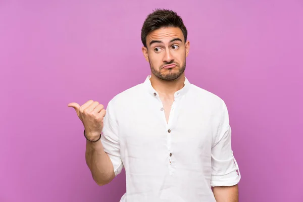 Guapo Joven Sobre Aislado Fondo Infeliz Señalando Lado — Foto de Stock