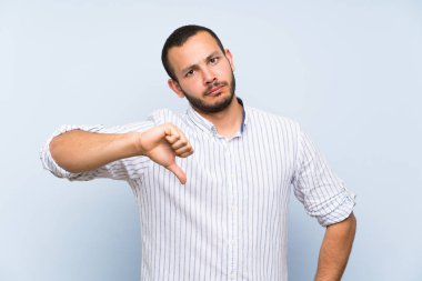 İzole mavi duvar üzerinde Kolombiyalı adam aşağı negatif ifade ile başparmak gösteren