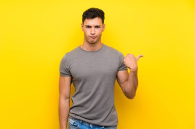 Izole sarı duvar üzerinde Yakışıklı adam mutsuz ve yan işaret