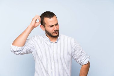 İzole mavi duvar üzerinde Kolombiyalı adam kafa çizilirken şüphe sahip