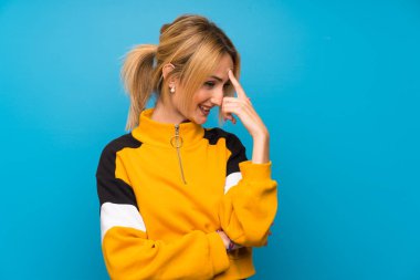 Soyutlanmış mavi arka planda genç sarışın kadın gülüyor.