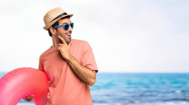 Onun yaz tatili ayakta ve sahilde çene el ile tarafa bakarak şapka ve güneş gözlüğü ile adam