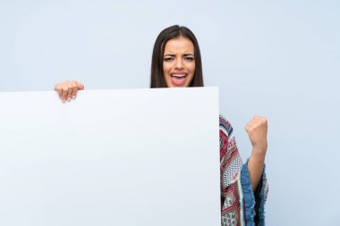 Bir kavram eklemek için boş beyaz bir pankart tutan izole mavi duvar üzerinde genç kadın