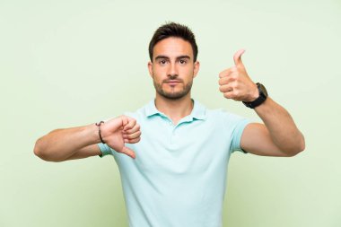İzole arka plan üzerinde yakışıklı genç adam iyi-kötü işareti yapma. Evet ya da değil arasında kararsız