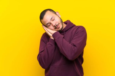 Sarı duvar üzerinde Sweatshirt ile Kolombiyalı adam aşkım ifade uyku jest yapma