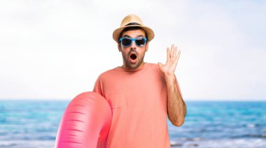 Sürpriz ve şok yüz ifadesi ile onun yaz tatili üzerinde şapka ve güneş gözlüğü ile adam. Ağız açık çünkü sahilde ne olduğunu beklemek değil