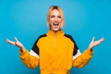 İzole mavi arka plan üzerinde genç sarışın kadın mutsuz ve bir şey ile sinirli