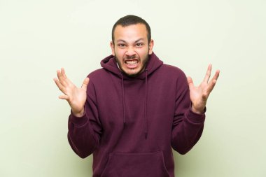 Yeşil duvar üzerinde Sweatshirt ile Kolombiyalı adam mutsuz ve bir şey ile sinirli