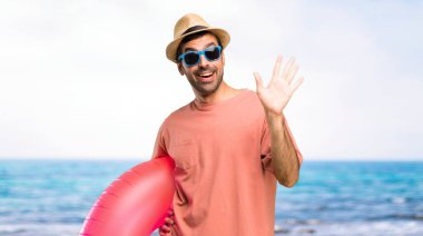 Sahilde mutlu ifade ile el ile selamlayan yaz tatilinde şapka ve güneş gözlüğü ile adam