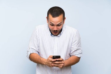 İzole mavi duvar üzerinde Kolombiyalı adam şaşırttı ve bir mesaj gönderme