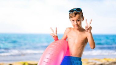 Yaz tatilinde çocuk gülümseyen ve sahilde zafer işareti gösteren
