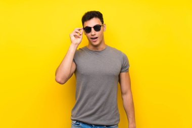 Gözlüklü izole sarı duvar üzerinde Yakışıklı adam ve şaşırttı