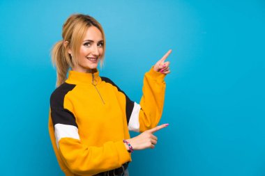 İzole edilmiş mavi arka planda genç sarışın bir kadın var.