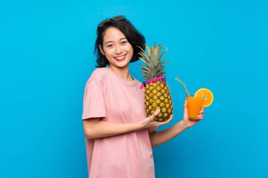 Güneş gözlüğü ile bir ananas tutan izole mavi arka plan üzerinde Asya genç kadın