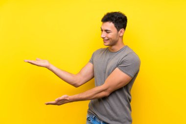 Izole sarı duvar üzerinde yakışıklı adam gelmeye davet için yan ellerini uzatan